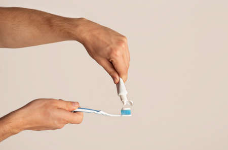 Young guy applying paste from tube onto toothbrush against light background, copy space. Panorama