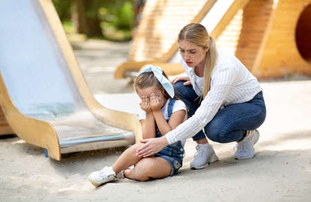 Mother Examining Daughters Injured Knee After Ride On Dangerous Slide In Park.