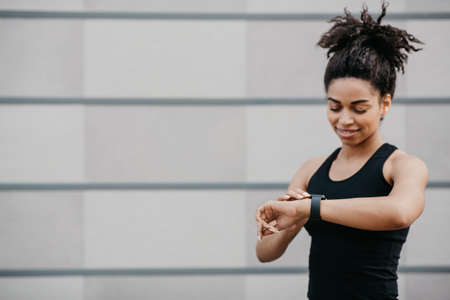 Smiling african american girl in sportswear checks fitness tracker and happy with result, copy space