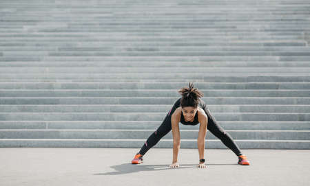 Exercises for flexibility outdoor. Joyful african american girl in sportswear with fitness tracker...