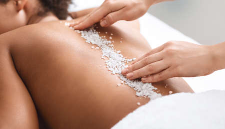 Closeup of therapist hands applying sea salt on black woman spine, healthcare and spa concept