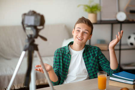 Cheerful guy teenager broadcasting from home, sharing his thoughts with followers, using cameraの写真素材
