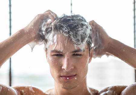 Closeup frontal portrait of handsome man washing hair with shampoo in the bathroom