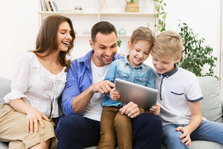 Parents And Kids Using Digital Tablet Sitting On Sofa Together At Home. Family Fun Concept