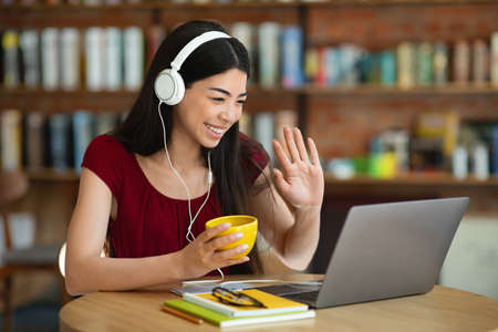 Video Call. Friendly Asian Girl In Headset Using Laptop At Cafe, Waving Hand At Camera, Free Spaceの写真素材