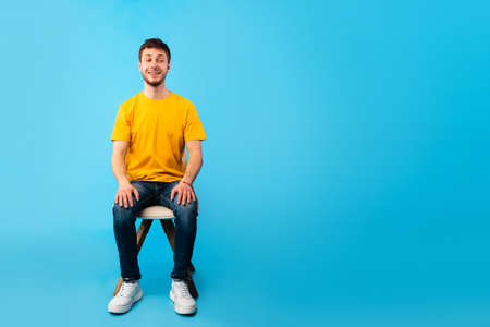 Casually Handsome. Studio shot of young man sitting on the chair and looking aside at copy space, blue wallの写真素材