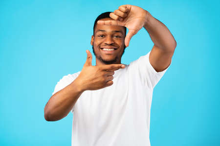 Frame The Moment. Smiling African American Man Framing Face With Fingers Looking At Camera Posing On Blue Studio Background.の写真素材