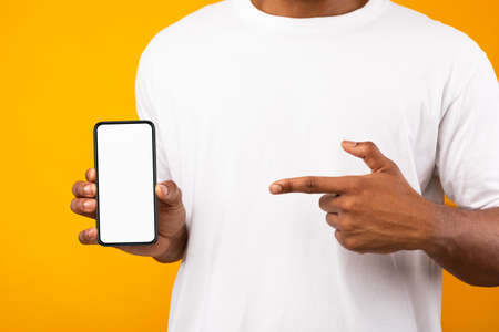 Black Man Showing Smartphone With Blank Screen Recommending Mobile App On Yellow Background. Mockup,...