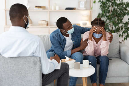 Caring Husband Comforting Black Wife Having Mental Health Problems After Coronavirus, Sitting At...