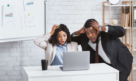 Black colleagues looking at laptop screen in terror, finding mistake in business project at modern...