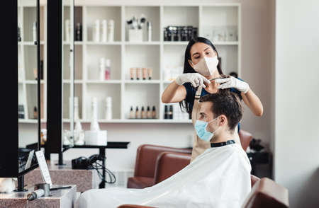 Safe visit to hairdressing salon. Hairdresser and client in protective medical masks, empty spaceの写真素材