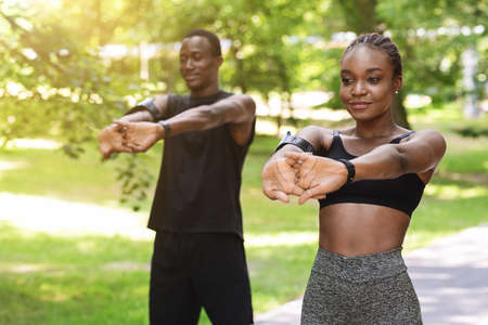 Healthy Lifestyle Concept. Black millennial couple doing sport outdoors together, stretching arm...