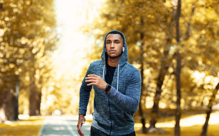 Handsome black sportsman in hoodie running outdoors on autumn day, panorama
