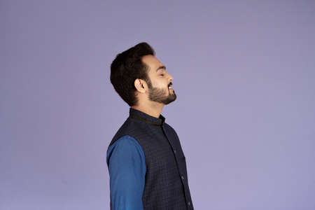 Side view of peaceful Indian man with closed eyes relaxing over lilac background