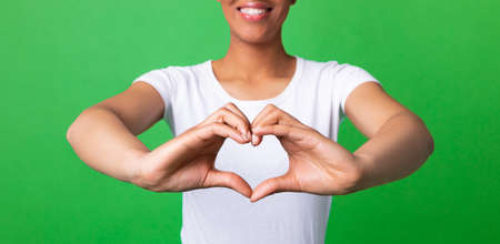 Closeup cropped view of smiling black woman shaping hands like heart on green background, panorama, bannerの写真素材