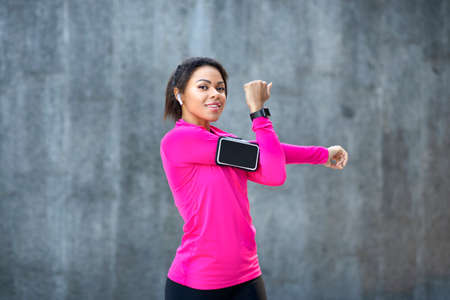 Pretty african girl stretching arms before training at park, grey stone background