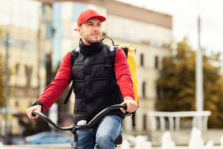 Courier Guy In Uniform Sitting On Bicycle Delivering Food In Urban Area Outside. Free Space For Textの写真素材