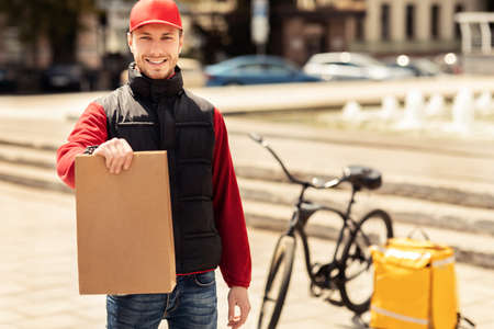 Your Offer. Courier Guy Holding Package Smiling To Camera Delivering Food Standing In Urban Area Outside. Free Space For Textの写真素材