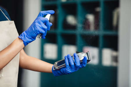 Barber disinfecting trimmer with disinfectant before cutting customer, personal safety concept,...