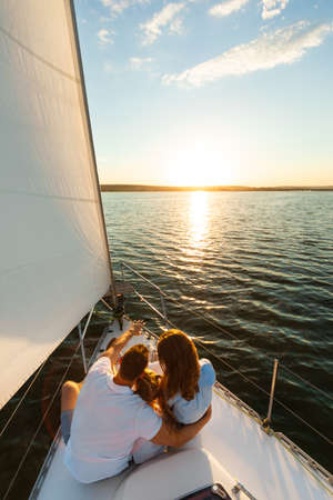 Family Sitting On Yacht Deck Back To Camera Enjoying Sailboat Ride In Sea On Summer Day. Sailing...