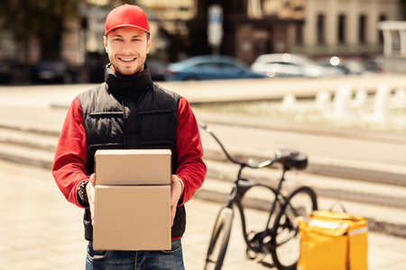 Fast Delivery. Happy Courier Holding Boxes Smiling To Camera Delivering Parcels In City. Blank Spaceの写真素材