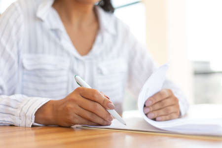 Business Accountant. Unrecognizable lady signing papers sitting at the wooden table
