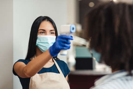 Epidemic prevention. Beauty salon worker checking client body temperature before procedures