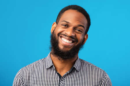 Positive Emotion. Cheerful african man smiling on blue isolated background, studio shot, closeup...