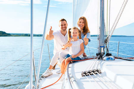 We Like Yachting. Family Gesturing Thumbs-Up Sitting On Sailboat Deck Sailing Across Sea Outside, Smiling To Camera.の写真素材