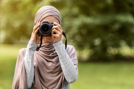 Unrecognizable muslim woman photographer taking photos at park, copy space