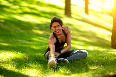 Happy black sporty girl stretching muscles, exercising at public park, empty space