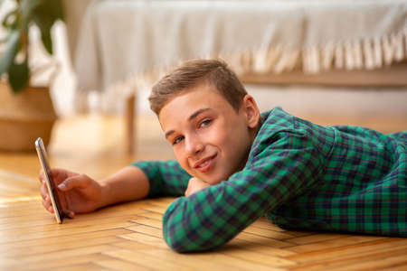 Smiling teenager laying on floor at home, using mobile phone, side view