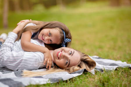 Cute Mother And Little Daughter Embracing Posing Smiling To Camera Having Picnic Lying On Blanket In Park. Free Spaceの写真素材
