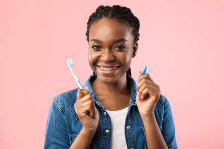 Teeth Hygiene. Black Woman With Brackets Holding Toothbrushes For Tooth Cleaning Posing On Pink...