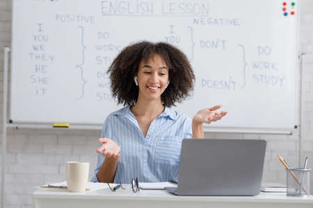 Easy english lessons at home. Friendly african american woman with wireless headphones looks at...