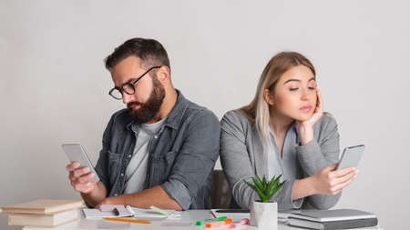 Smartphone addiction at work. Man and woman turned away from each other and look at smartphones at table in office,panorama, copy spaceの写真素材