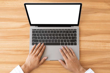 Workspace with hands typing on laptop with blank screen. Flat lay, top view, wooden tableの写真素材