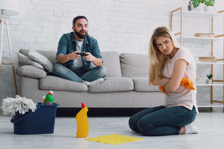 Housewife and lazy husband. Offended woman folding her hands with gloves on chest and does not want...