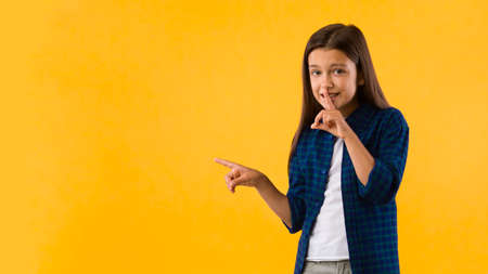 Secret Back-To-School Sales. Little girl pointing aside at copyspace and putting her finger on lips...