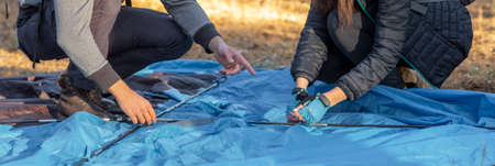 Cropped of two people setting up tent in forest, panorama, hiking, camping conceptの写真素材