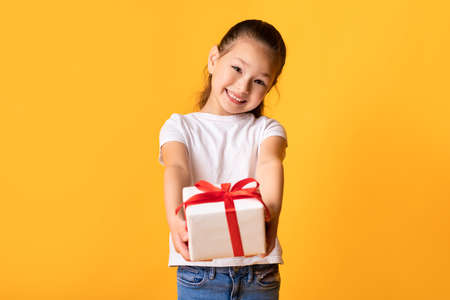 Its For You. Portrait of cute asian girl holding present and giving box to camera, yellow wallの写真素材