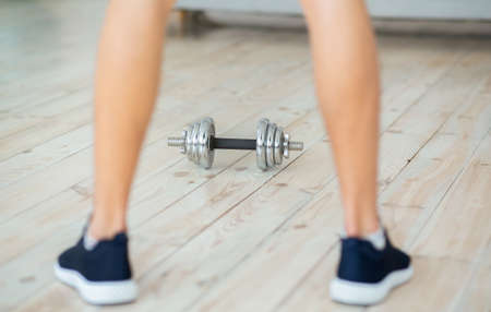 Strength training during quarantine. Man in sneakers stands near dumbbell and cup for shakes,...