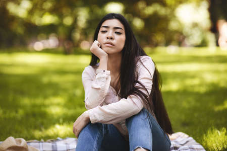 Summertime Sadness. Portrait Of Pensive Asian Woman Sitting On Plaid In Park, Resting Head On Hand, Thinking About Something, Copy Spaceの写真素材