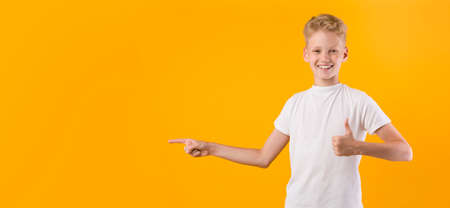 Check This. Smiling boy pointing his finger aside at copyspace and showing thumb up isolated over...