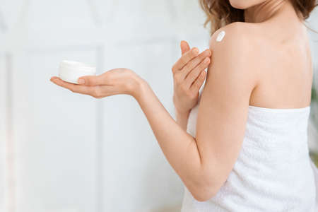 Unrecognizable woman holding jar, applying cream on her body after shower, home interior, copy spaceの写真素材