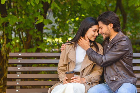 Young couple in love sitting on bench at park and cuddling, copy space