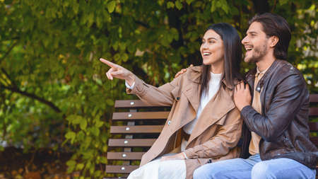 Emotional pretty girl showing something her boyfriend at park, pointing at copy space, panorama