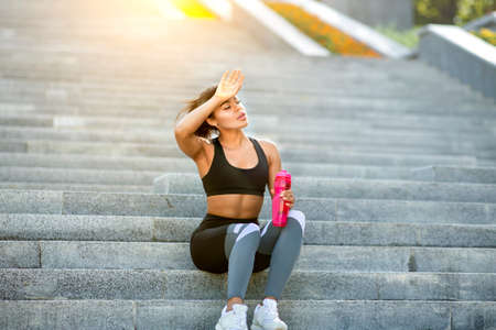 Tired african girl runner resting on stairs at park, drinking water, copy spaceの写真素材