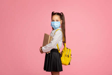 School during quarantine. Small child in uniform with books, backpack and protective mask, isolated on pink background, free spaceの写真素材