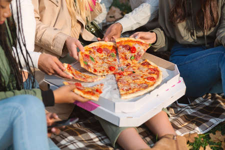 Close up of take away pizza and multiethnic teenagers hands, youngsters having picnic outdoors